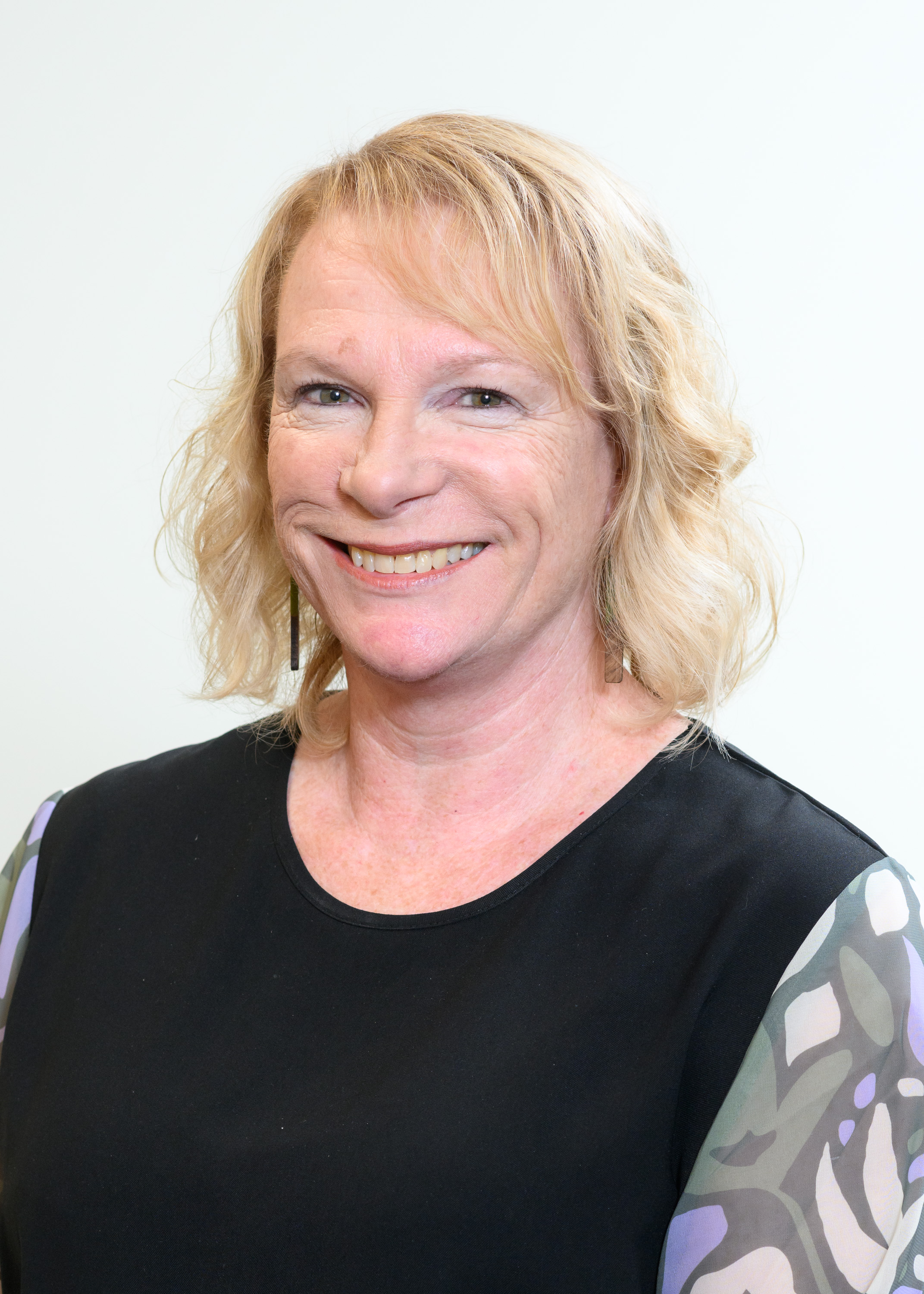 Portrait of Lauren Prosser, Kaiwhakahaere Kaupapahere, Rangahau, me te Mahinga – Director of Policy, Research and Performance, wearing a black sleeveless top with patterned sleeves, photographed against a plain light background.