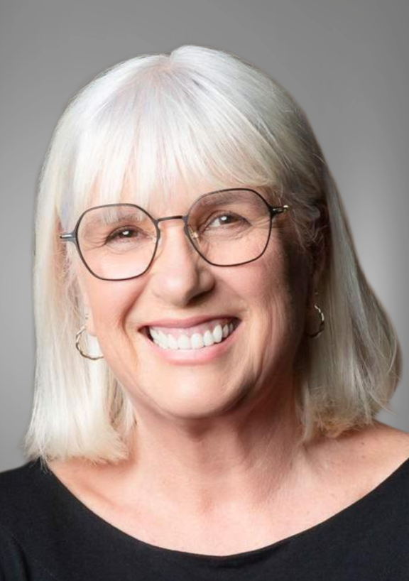 Portrait of Dr Sharon Brownie, Deputy Chairperson, photographed against a plain background, wearing a dark top and light‑coloured hair styled to shoulder length.