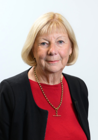 Helen Nielsen, head‑and‑shoulders studio portrait wearing a red top, black jacket and a gold necklace, against a plain white background.
