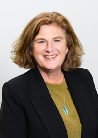 Portrait of Catherine Byrne, Pouārahi/Pouroki – Chief Executive/Registrar, wearing a black blazer over an olive‑green top and a greenstone pendant necklace, photographed against a plain light background.